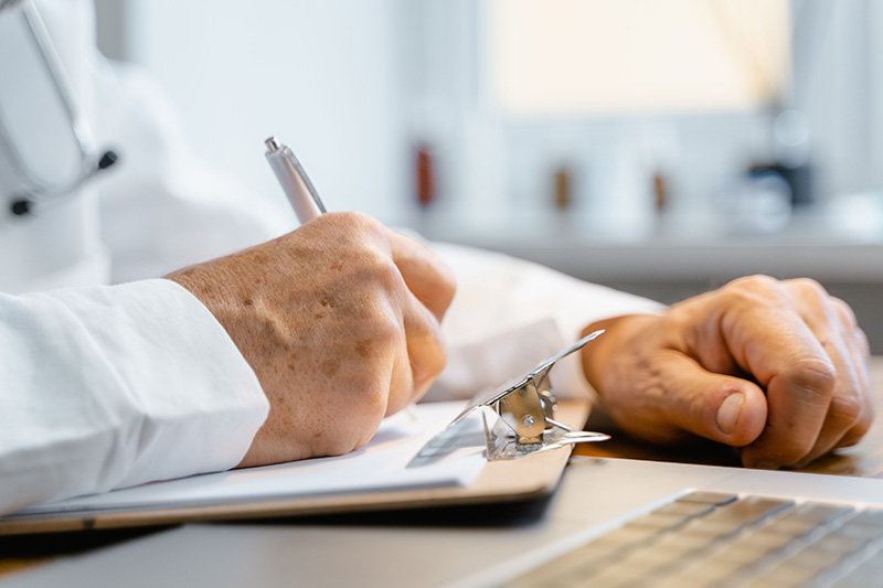 A doctor recording clinical notes on a clipboard at their desk
